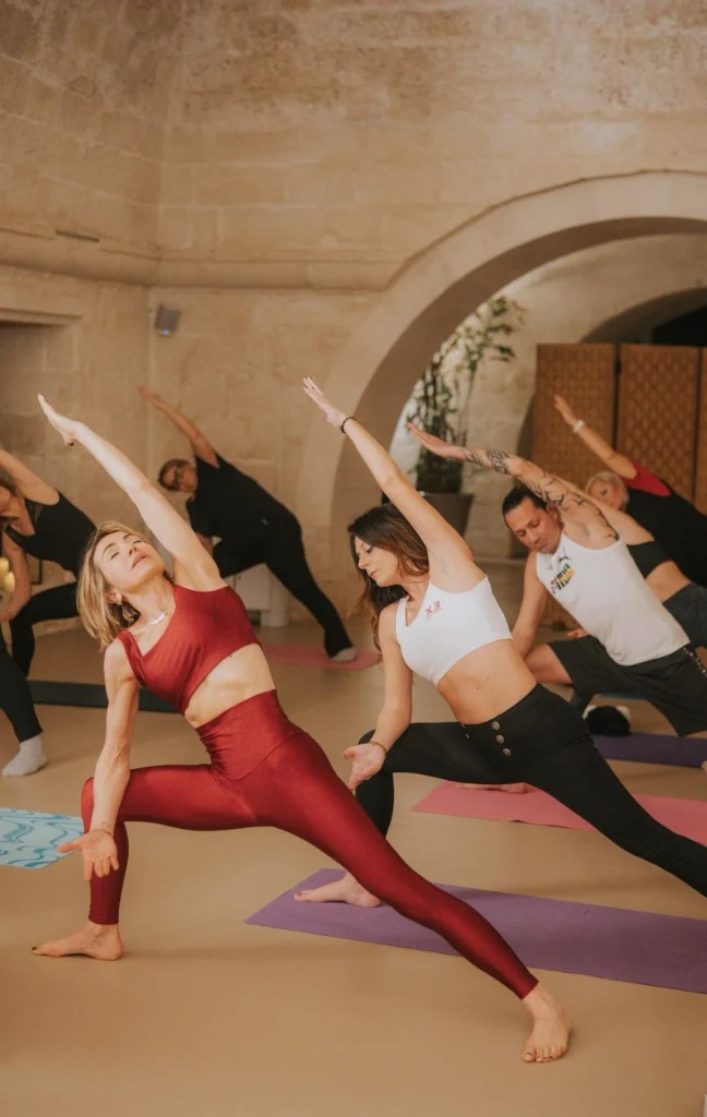 Un gruppo pratica yoga sui tappetini in una sala con pareti e archi in pietra.