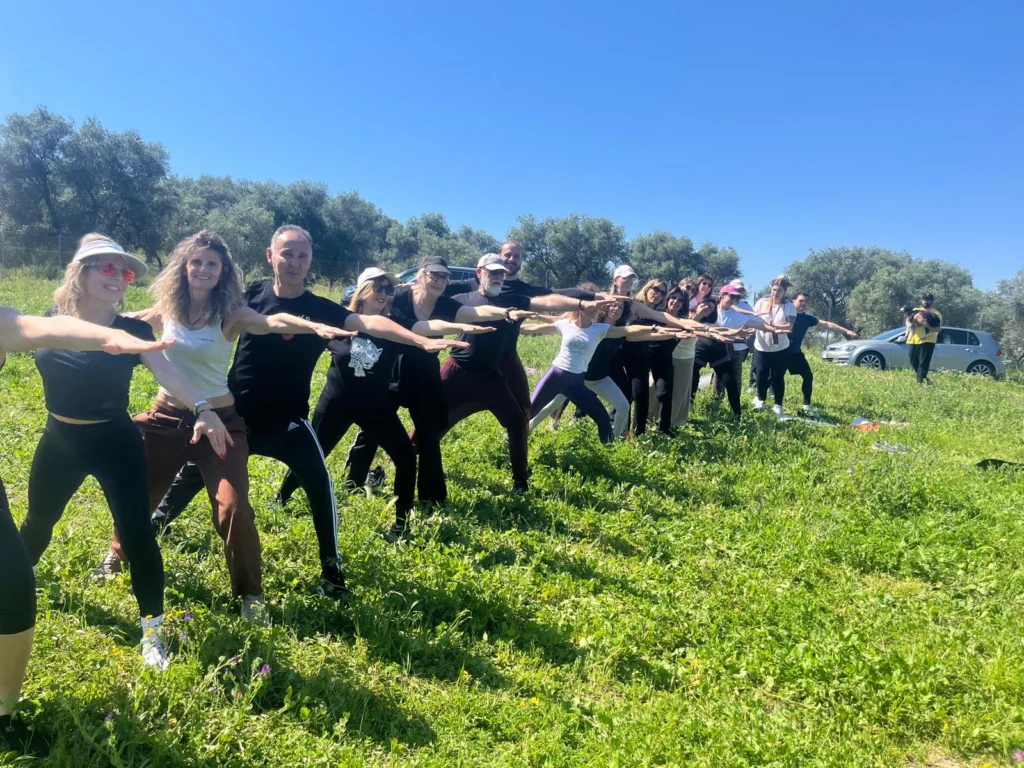 Un gruppo pratica yoga sull’erba, con le braccia distese davanti agli alberi.